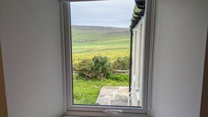 Habitación con ventana que da a un campo verde y un sendero de piedra.