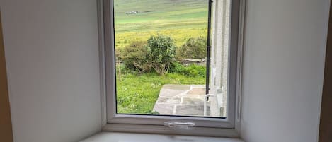 A room with a window overlooking a green field and stone pathway.