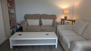 Una sala de estar con un sofá, una mesa de centro, una mesita de noche con una lámpara y una estantería.
