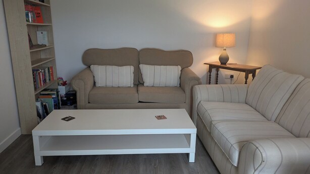 A living room with a sofa set, a coffee table, a side table with a lamp, and a bookshelf. - Lower Cottage (Rousay)