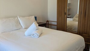 A neatly made bed with white linens and towels, a wooden wardrobe, and a small bedside table. - Lower Cottage (Rousay)