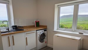 Una cocina con lavadora, un radiador y una ventana que da a la campiña.