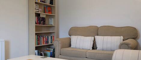 A living room with a beige sofa, a bookshelf, and a white coffee table.