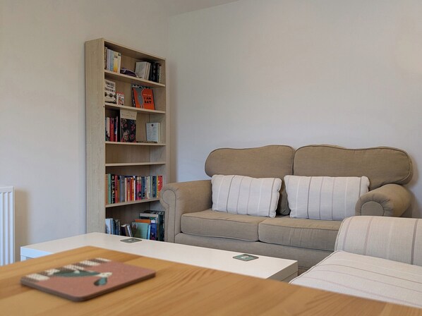 A living room with a beige sofa, a bookshelf, and a white coffee table.