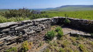 A stone wall with a view of a rural landscape, including a house and open fields. - Lower Cottage (Rousay)