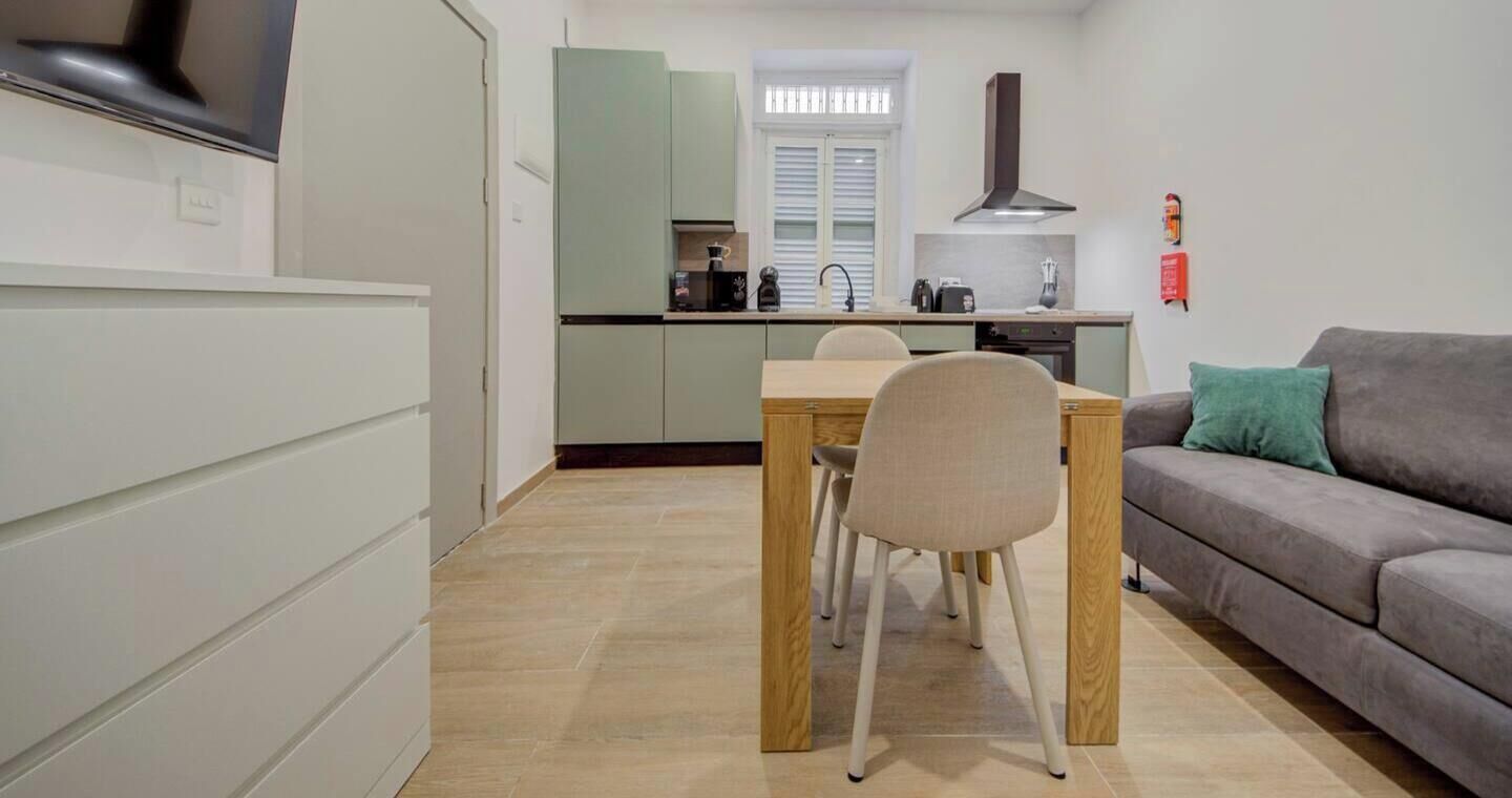 Une cuisine compacte avec une table et des chaises, un canapé gris et un téléviseur sur le côté gauche.