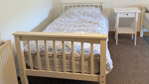 A single bed with a white headboard and footboard, a bedside table, and a radiator.
