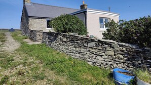 A stone house with a stone wall and a blue wheelbarrow.