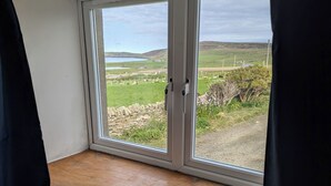 A room with a large window overlooking a rural landscape, a stone wall, and a wooden ledge.