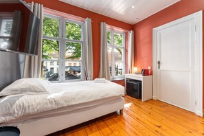 Una habitación con cama, escritorio, puerta y ventanas amplias.