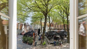 Uitzicht door een raam op een levendige openbare markt met kraampjes en voetgangers.