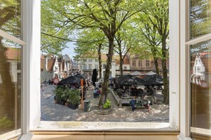 Blick durch ein Fenster auf einen belebten Markt mit Ständen und Fußgängern.