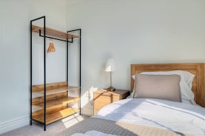 Ein Schlafzimmer mit einem Bett, einem Nachttisch, einem Holzregal und einer Pendelleuchte.
