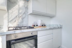 A kitchen with a gas stove, oven, white cabinets, and a marble backsplash.