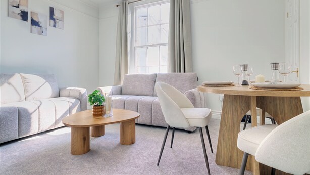 Ein modernes Wohnzimmer mit einer Couch, einem Couchtisch, einem Esstisch mit Stühlen und einem Fenster mit Vorhängen.