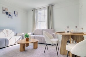 Una sala de estar moderna con un sofá, una mesa de centro, una mesa de comedor con sillas y una ventana con cortinas.