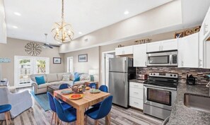 A modern kitchen with white cabinets, stainless steel appliances, and a dining area with blue chairs. - Laguna Cottage, Sleeps 10, Golf Cart + Beach Gear (Panama City Beach)