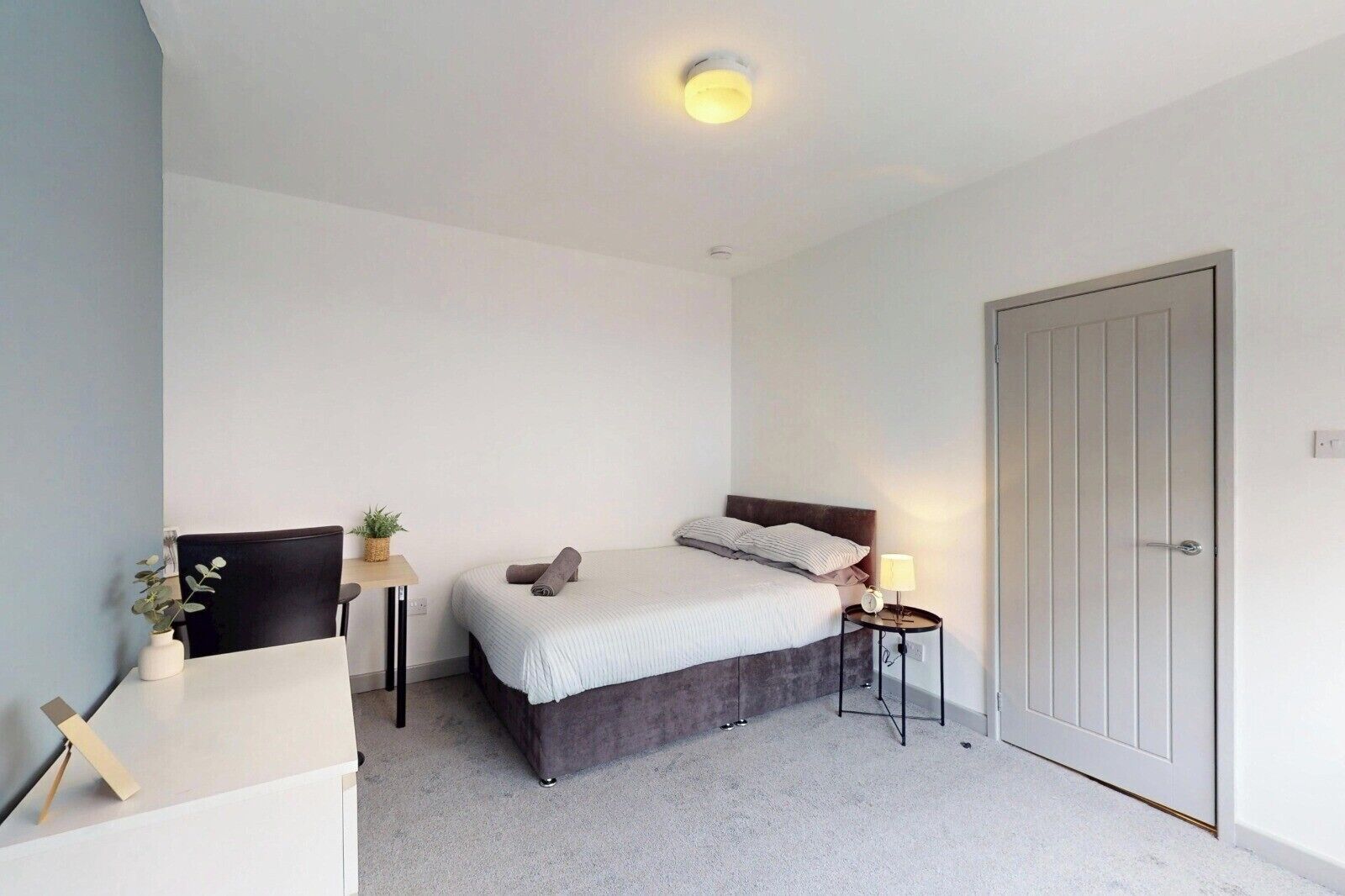 A bedroom with a bed, bedside table, lamp, and a door.