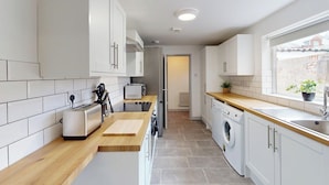 A modern kitchen with white cabinets, a wooden countertop, a built-in washing machine, and a window with a view. - House Sleeps 10 With Wifi (Sunderland)
