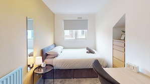 A bedroom with a bed, bedside table, lamp, and a window with blinds. - House Sleeps 10 With Wifi (Sunderland)