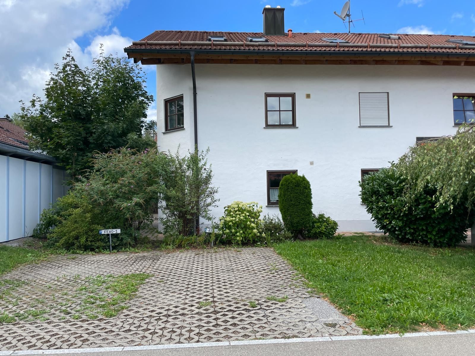 A two-story house with a tiled roof, a paved driveway, and a well-maintained lawn.