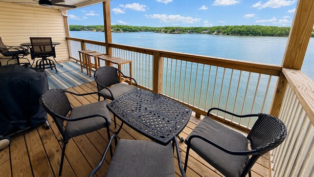A covered outdoor deck with wooden furniture, a ceiling fan, and a view of a lake. - Front Row to the Main Channel - 3BR walk in unit! (Osage Beach)