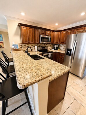 A kitchen with granite countertops, stainless steel appliances, wooden cabinets, and a central island with bar stools. - Front Row to the Main Channel - 3BR walk in unit! (Osage Beach)