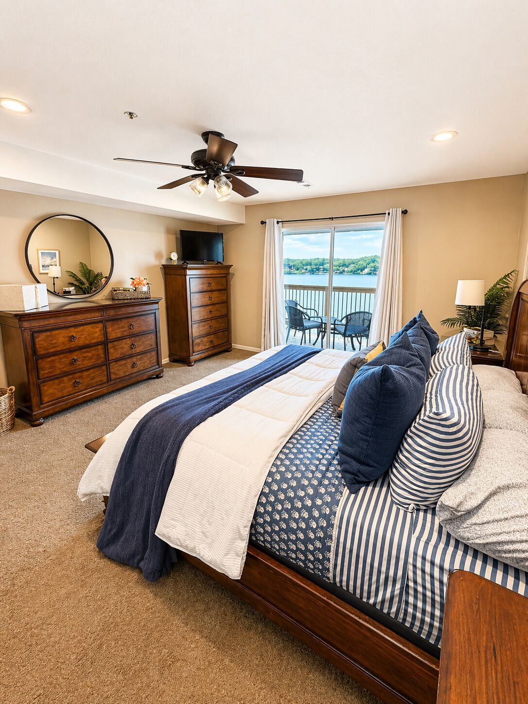 A bedroom with a bed, a dresser, a ceiling fan, a TV, and a balcony with chairs.