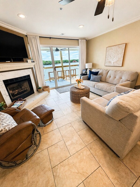 A living room with a fireplace, a sofa, a chair, a TV, and a view of the outdoors. - Front Row to the Main Channel - 3BR walk in unit! (Osage Beach)