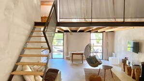 A loft-style room with a wooden staircase, a hanging chair, a flat-screen TV, and a large window. - Holiday Home 'L'Essentiel' with Shared Pool, Shared Garden and Wi-Fi (Lieuran-lès-Béziers)