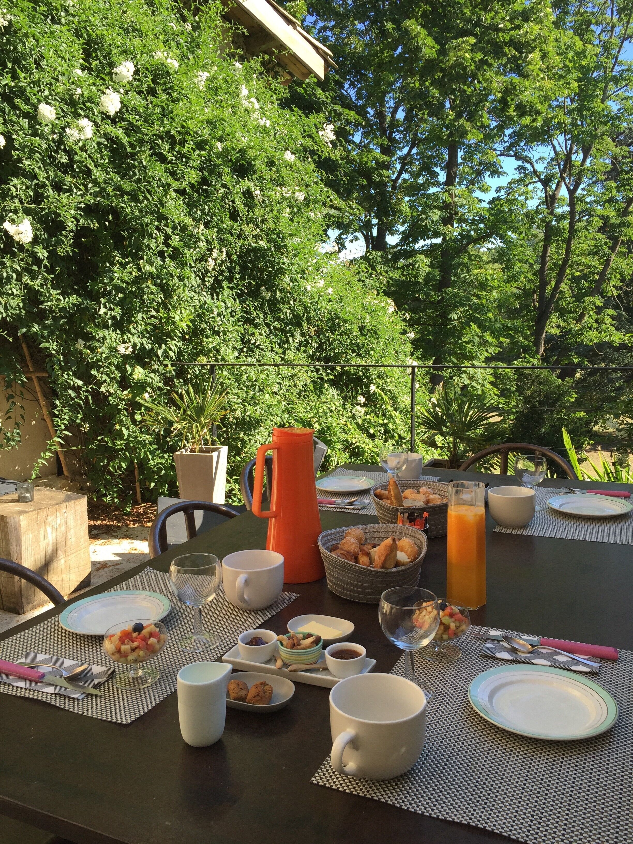 An outdoor dining area with a table set for breakfast, surrounded by lush greenery.