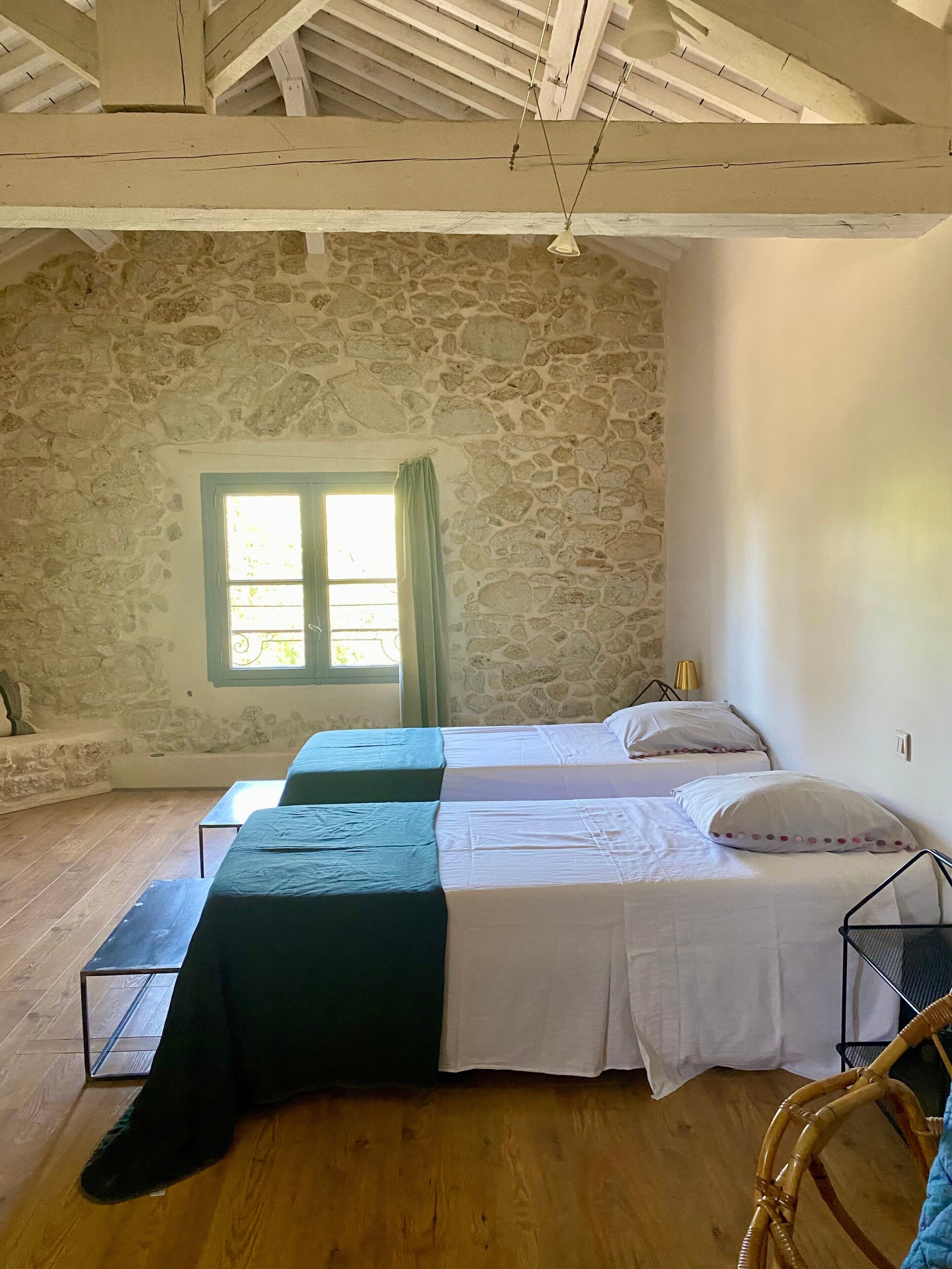 Une chambre avec deux lits, un mur en pierre, une fenêtre avec des rideaux et un plancher en bois.