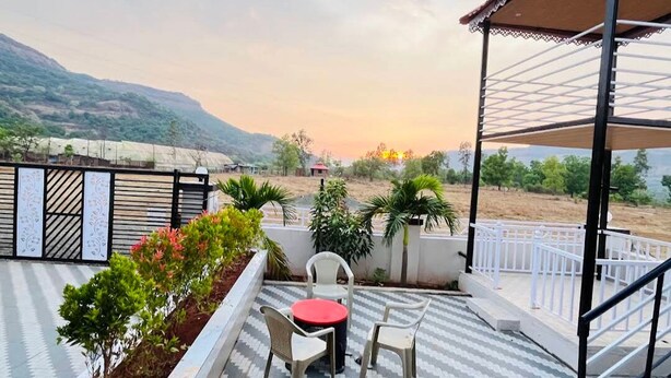 A terrace with a table and chairs, a view of the landscape, and a pergola structure. - Sanvi farmhouse. Hill view with waterfalls. (Thoran)