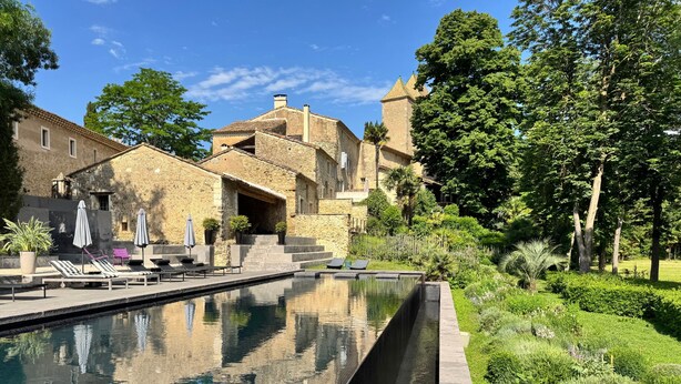A swimming pool with lounge chairs and umbrellas, a stone building with a tower, and lush greenery. - Holiday Home 'Présbytère' with Shared Pool, Shared Garden and Wi-Fi (Lieuran-lès-Béziers)