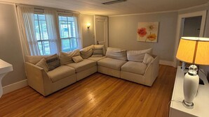 A living room with a beige sectional sofa, a wooden floor, a lamp, and a painting on the wall. - Spacious Home with fenced in yard, close to everything, great for families (Rutherfordton)