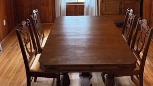 A wooden dining room with a table and chairs, a window with curtains, and a wooden cabinet. - Spacious Home with fenced in yard, close to everything, great for families (Rutherfordton)