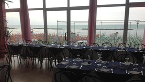 Un restaurante con mesas dispuestas para comer, amplias ventanas con vista al mar y un paisaje costero.