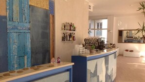 Zona de recepción con mostrador, estantes con botellas, máquina de café y espejo.