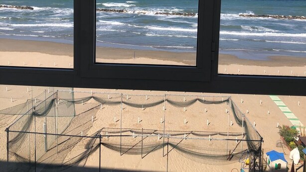 Vista de una playa a través de una ventana, mostrando arena y olas del océano.