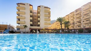 A swimming pool with a clear blue surface, surrounded by multi-story buildings with balconies and palm trees. - Home2Book Fresh Beach & Pool Apt Los Cristianos (Los Cristianos)