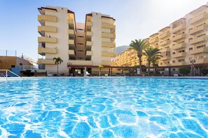Ein Swimmingpool mit glatter, blauer Wasseroberfläche, umgeben von mehrstöckigen Gebäuden mit Balkonen und Palmen.