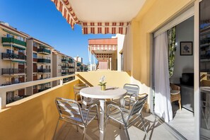 Ein Balkon mit rundem Tisch und Stühlen, einem Blumentopf und einem gestreiften Sonnensegel.