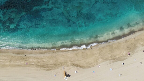An aerial view of a beach with clear turquoise water, sandy shore, and scattered people. - Home2Book Fresh Beach & Pool Apt Los Cristianos (Los Cristianos)