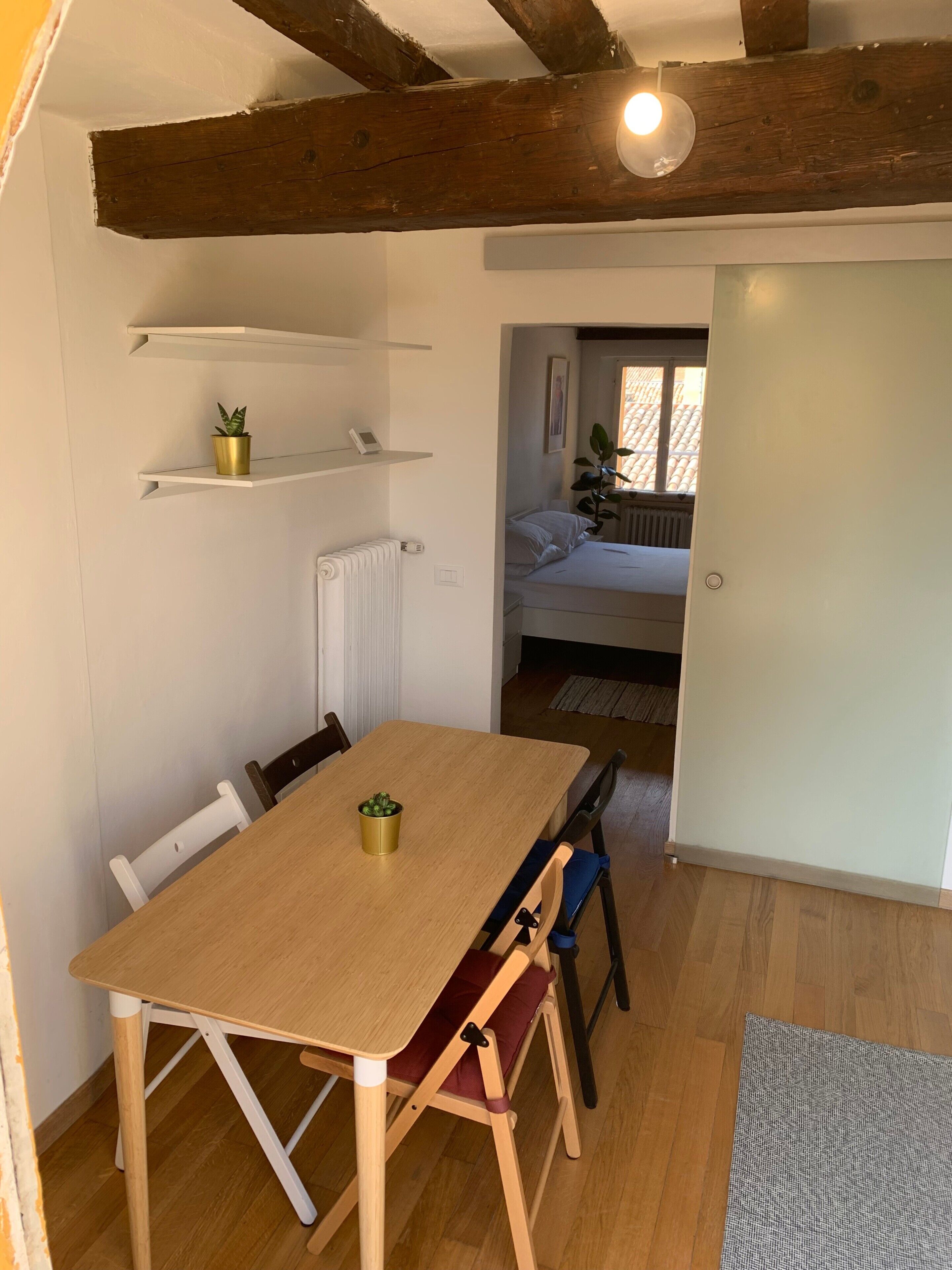 A dining area with a wooden table and chairs, a radiator, and a potted plant on a shelf.