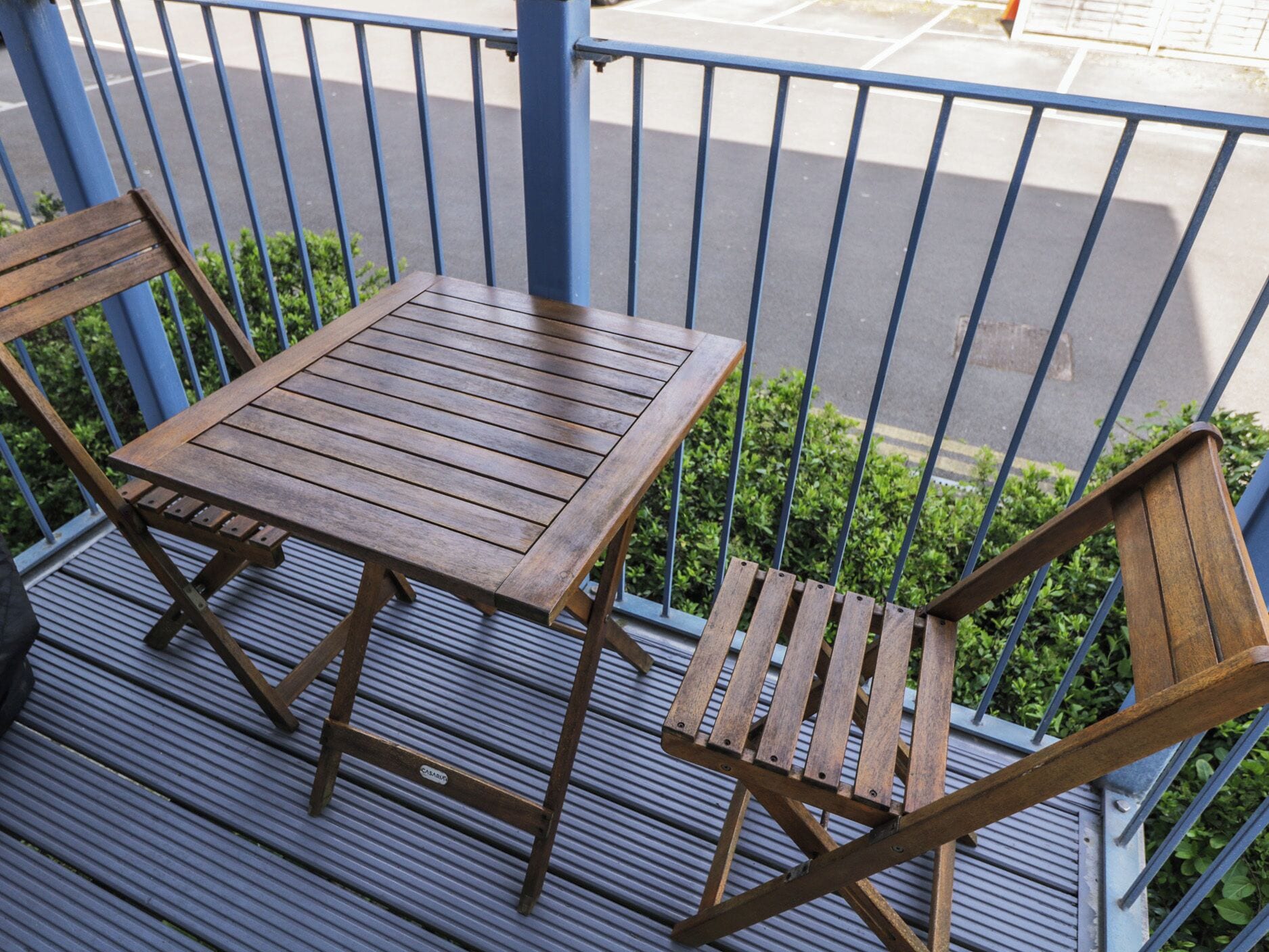 A wooden table and two chairs on a balcony with a metal railing.