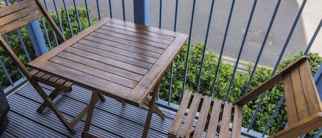 A wooden table and two chairs on a balcony with a metal railing.