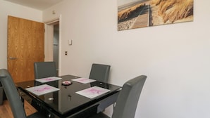 Un coin repas avec une table en verre, quatre chaises et une décoration murale sur le thème de la plage.