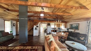 A spacious living area with a wooden ceiling, a sofa, a dining table, and a kitchen in the background.