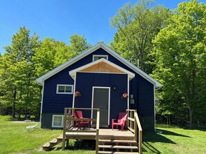 Une cabane bleue avec un porche, deux chaises rouges et une terrasse en bois.