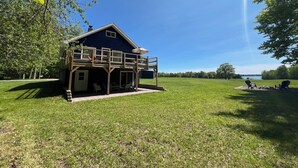 A blue house with a balcony, surrounded by a grassy field and trees.